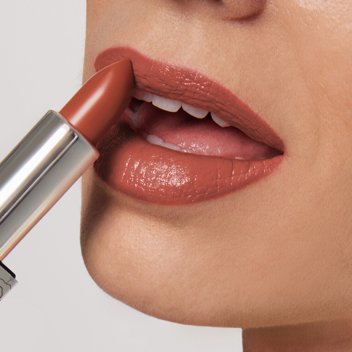 A close-up shows someone applying Shopgalaxyss 1975 Shiny Velvet Cream Lipstick #9, an ultra-creamy, brownish-red shade. It glides smoothly from the metallic tube onto slightly open lips, providing a glossy finish against a neutral background.