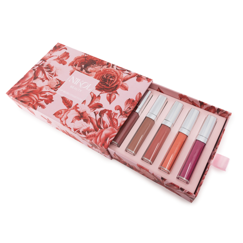 Nikol Beautys Lip Gloss Collection comes in a luxury gift box adorned with a pink floral pattern. Inside are five volumizing lip glosses in nude, pink, and purple shades, each with silver caps and arranged in individual compartments.