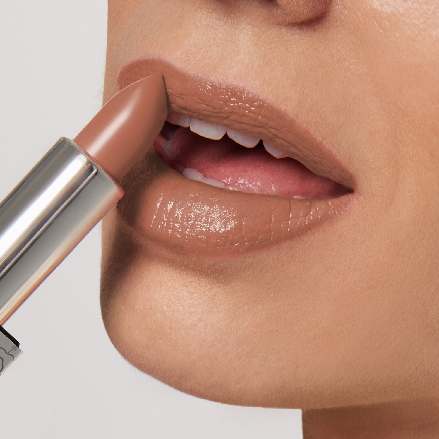 A close-up shows a person applying Shopgalaxyss Figure It Out Shiny Velvet Cream Lipstick #475, a vegan nude shade, to their lips. The lipstick comes in a metallic tube and gives their smooth, defined lips a glossy appearance with visible light reflection.