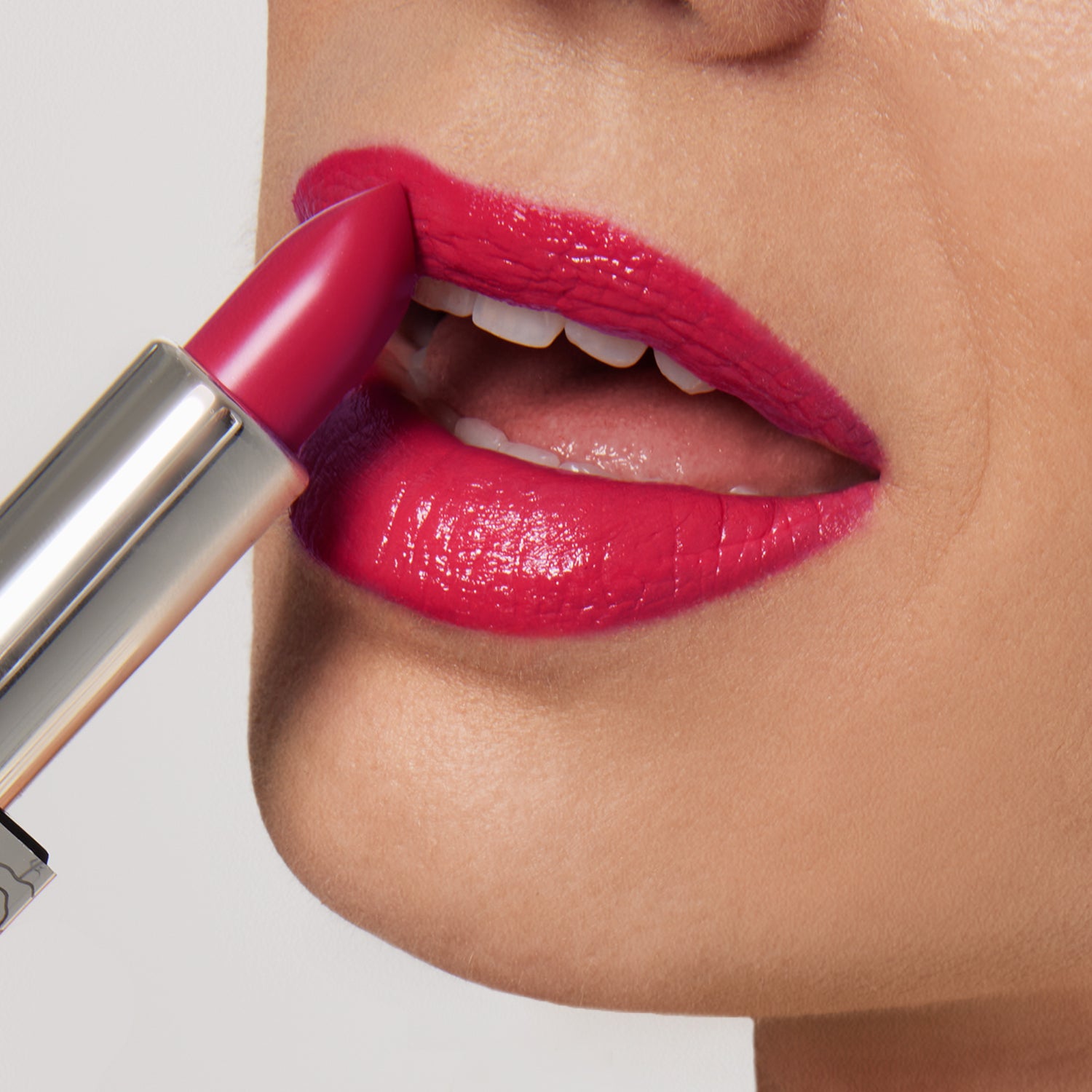 A close-up of someone applying Shopgalaxys’s Fleur Shiny Velvet Cream Lipstick #34, a vibrant pink vegan formula, showing smooth, glossy lips, white teeth, and part of the metallic lipstick tube.