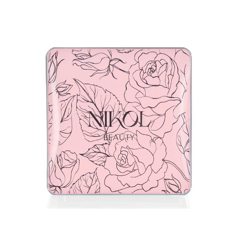 A light pink square compact with black floral rose and leaf designs features Shopgalaxys at the center. The Nikita Banana Brightening Powder delivers a flawless finish with its pressed powder formula.