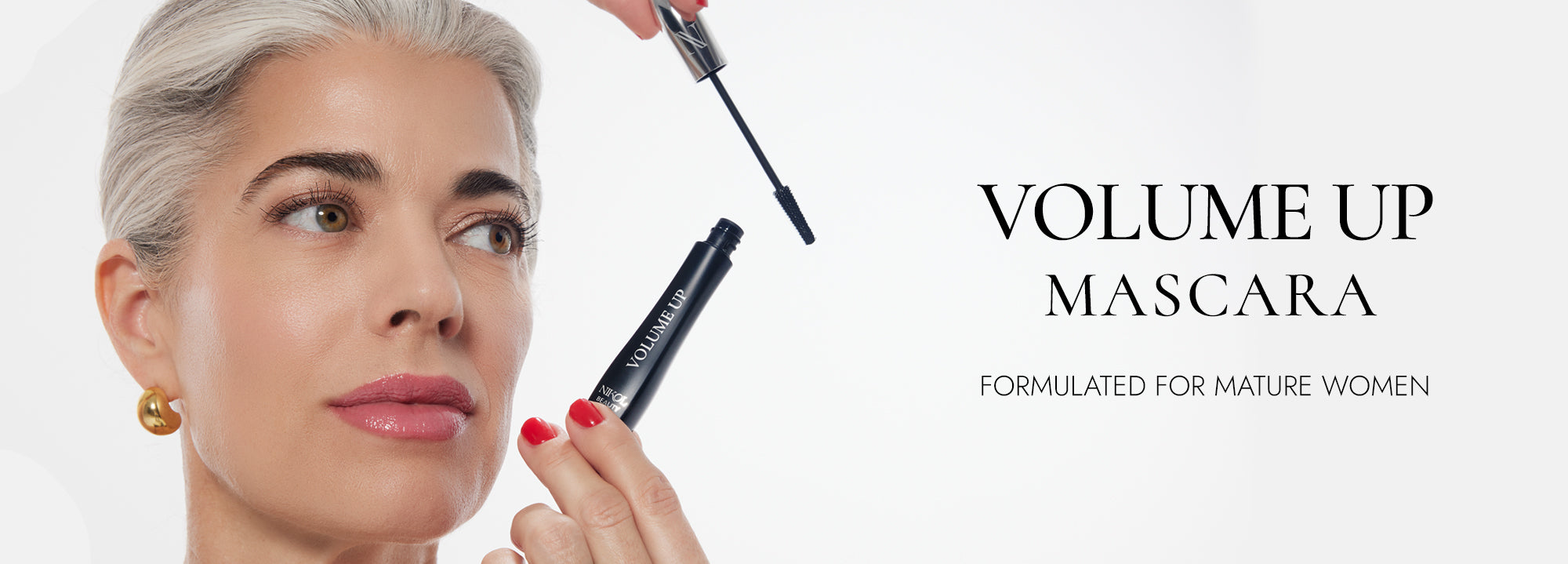 A woman with gray hair and gold earrings applies mascara, holding a black tube labeled VOLUME UP. The text beside her reads, VOLUME UP MASCARA—FORMULATED FOR MATURE WOMEN.