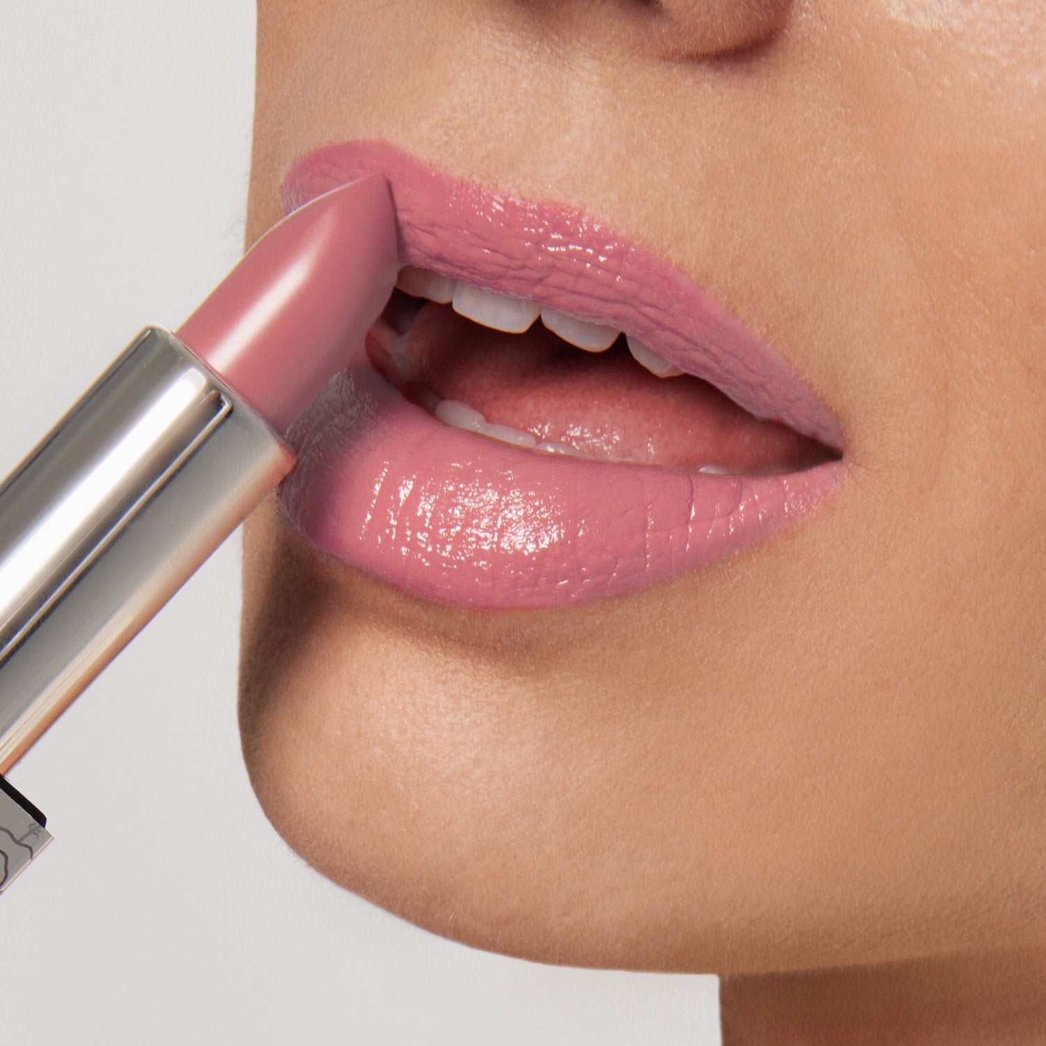 A person applies Shopgalaxyss Pretty Smart Shiny Velvet Cream Lipstick #337, showcasing its ultra-creamy pink finish. The metallic reflective case suggests its hydrating formula, with slightly parted lips revealing a hint of white teeth against a neutral gray background.