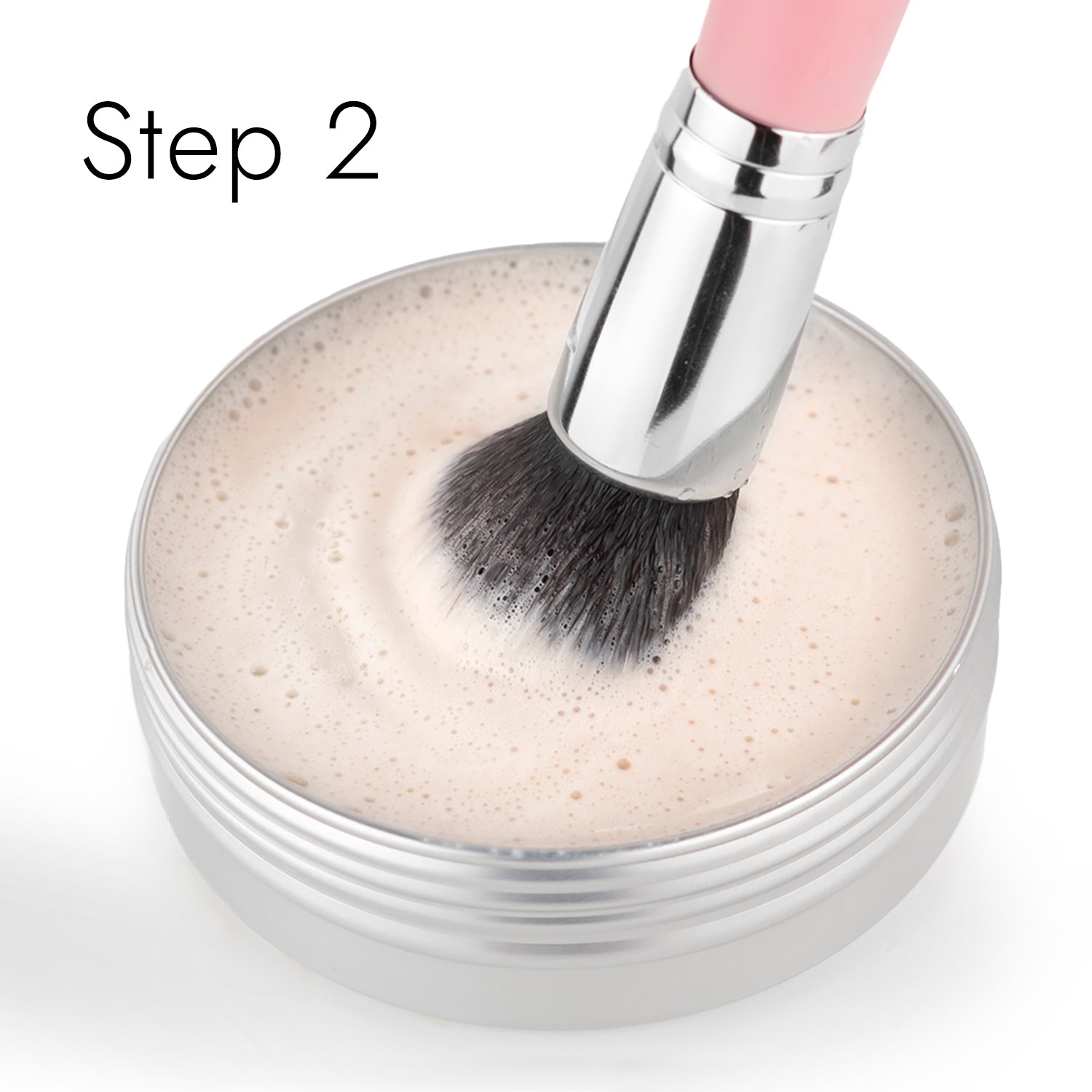 A makeup brush swirls in a round container filled with light-colored soapy water, revitalized by Shopgalaxyss Lux Brush Soap. The words Step 2 adorn the upper left corner.