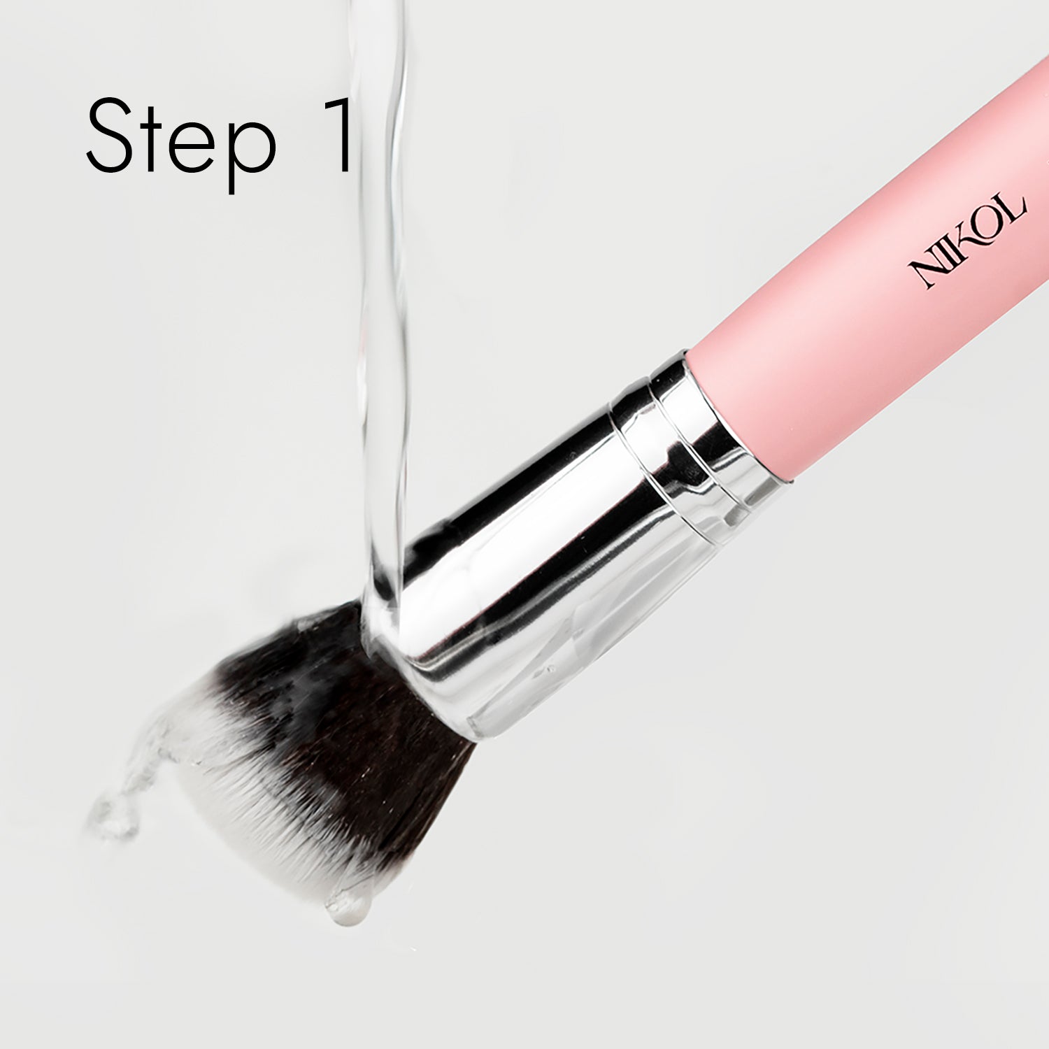 A pink-handle makeup brush with a silver ferrule is washed under running water, its bristles glistening wet. The process begins with Shopgalaxyss Lux Brush Soap enriched with coconut oil. Step 1 is displayed in the top left corner.