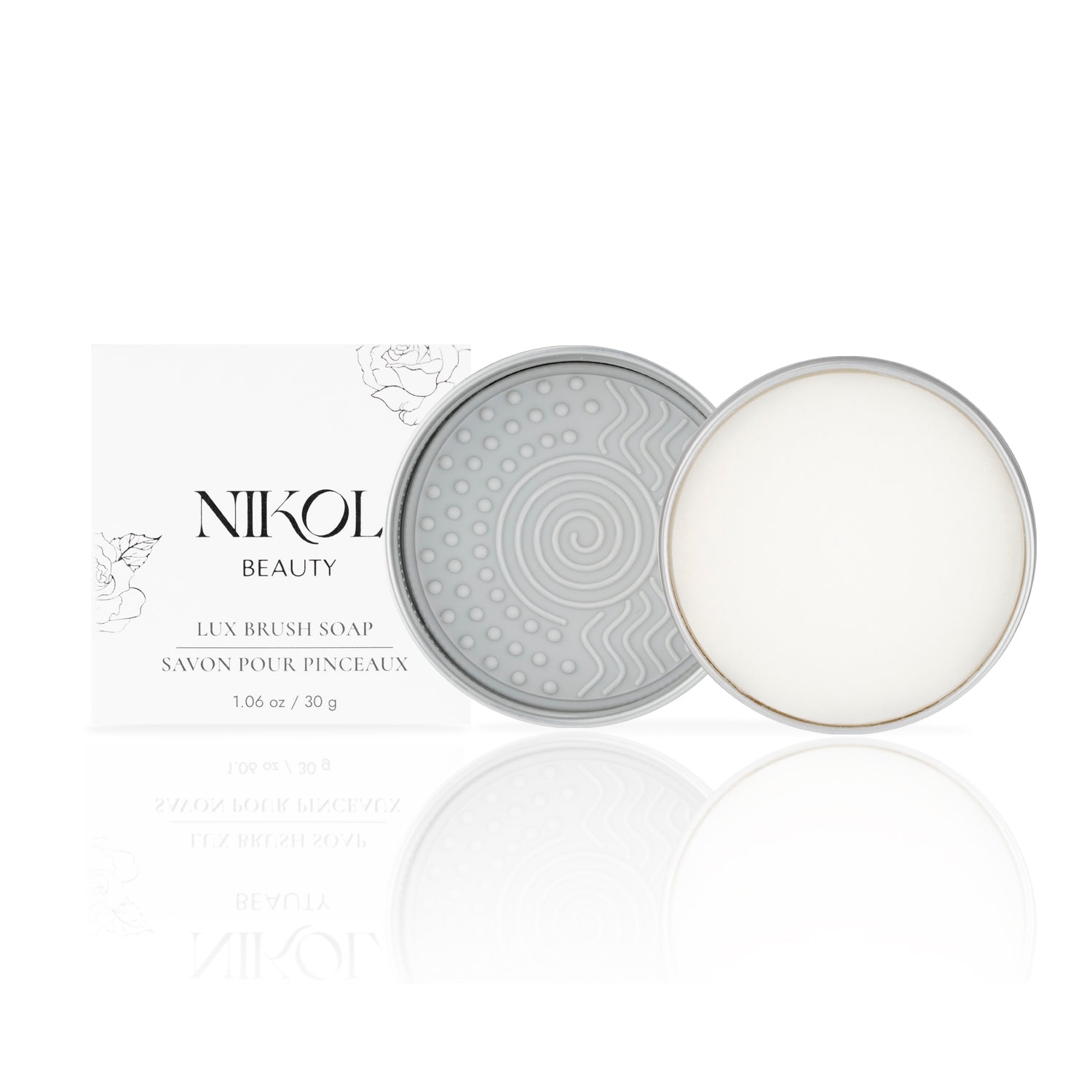 A cleaning pad and coconut oil-infused white soap sit in a round open container. Behind it, a white box with Shopgalaxys and Lux Brush Soap alongside floral designs glimmers on the glossy surface, ready to cleanse your makeup brushes.