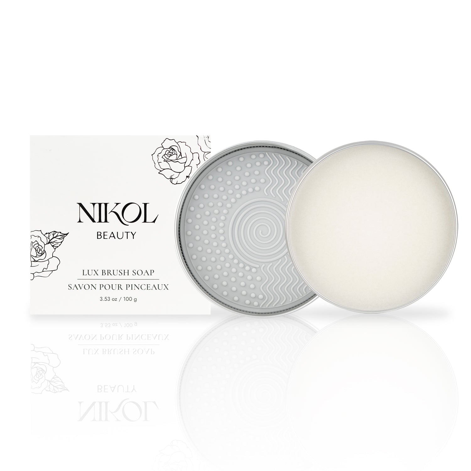 A cylindrical tin with a textured geometric lid holds a round bar of Lux Brush Soap by Shopgalaxys next to its white packaging adorned with floral line art. Infused with coconut oil, the soap gently cleans makeup brushes.