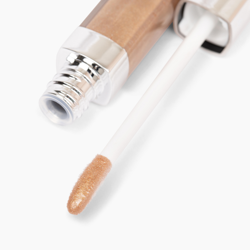 A close-up of Shopgalaxyss Manifest & Glow #183 lip gloss tube reveals its gold glitter finish and nourishing avocado oil benefits. The applicator wand is partially out, showing the shiny metallic product tip. Sleek packaging boasts a reflective cap.
